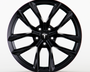 A black Tesla wheel rim with a sleek, multi-spoke design is shown in a clean, white studio setting. The central hub cap features the Tesla logo prominently.