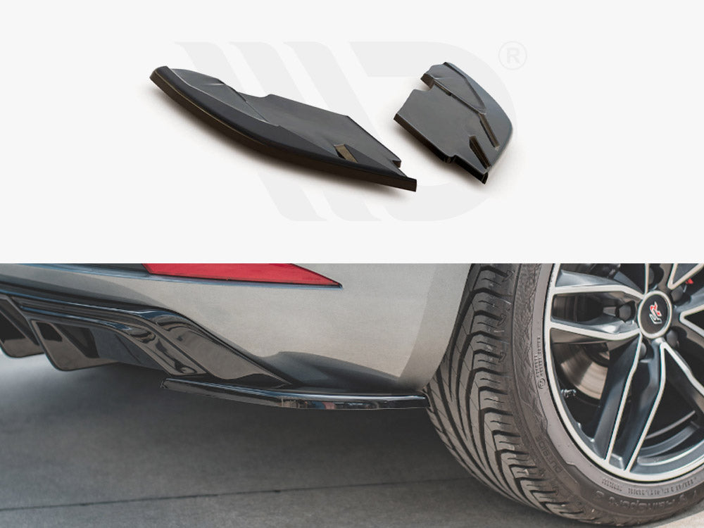 Two black aerodynamic car parts are shown above a rear view of a car. The car's rear diffuser and tire are visible on a concrete surface.