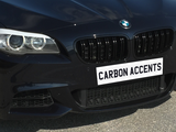 A black car features carbon accents on its front grille, parked on a paved surface. Text on the license plate area reads 