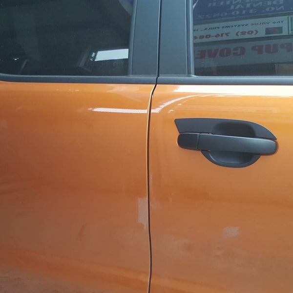 Orange car doors with black handles are closed, reflecting nearby objects. A sign with text is visible through the window.