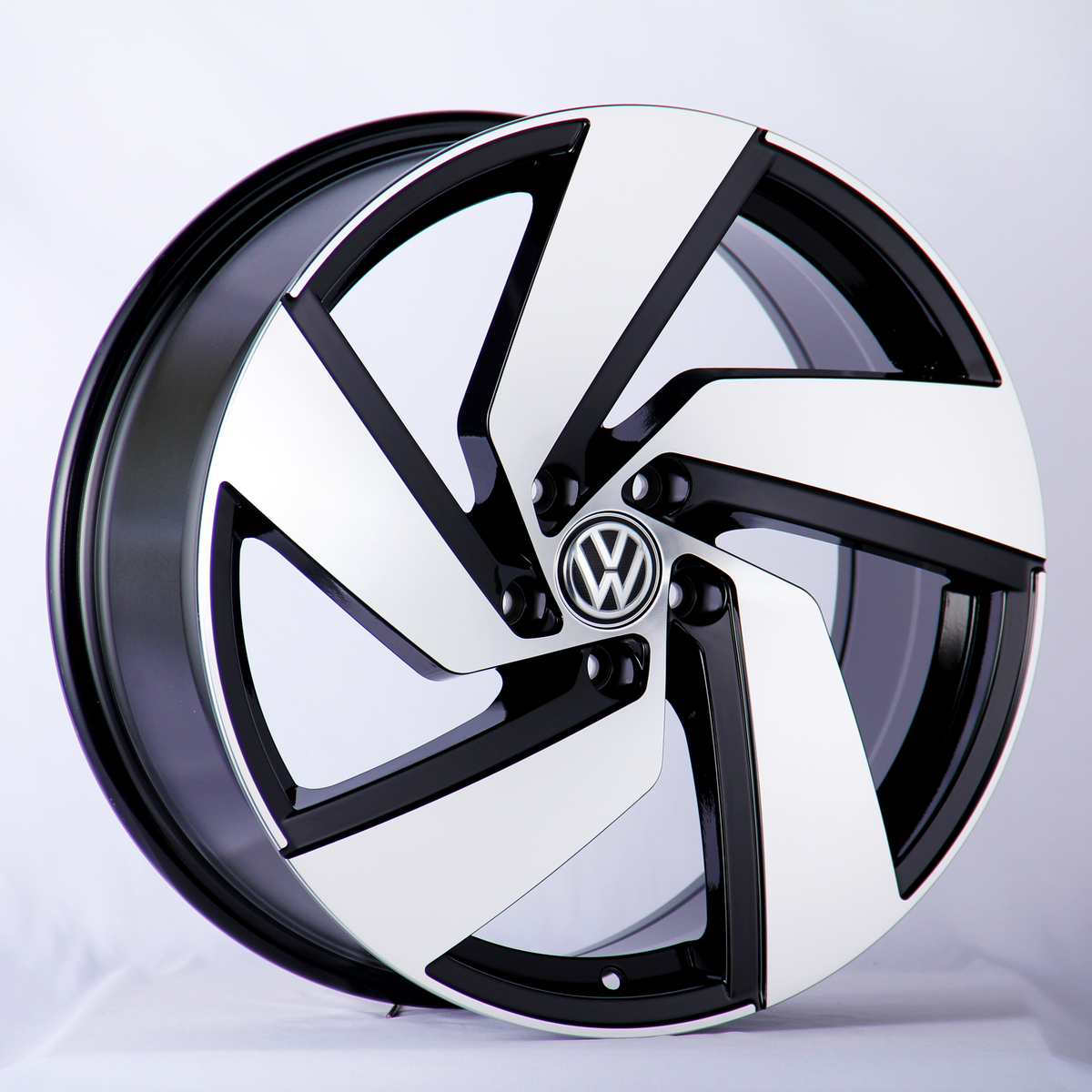 A car wheel rim displays a black-and-white geometric spoke design with a Volkswagen logo at the center, set against a plain white background.