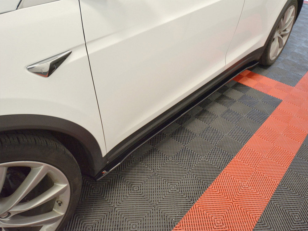 A white car is parked, showcasing sleek side skirts, on a checkered floor composed of red and gray tiles in a garage setting.