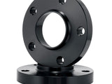 A black metal flange with multiple bolt holes rests on another flange against a plain white background, suggesting an industrial or mechanical setting.