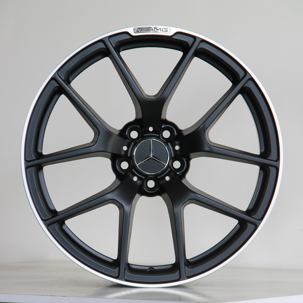 A black alloy wheel with a Mercedes logo in the center and "AMG" label on the rim, resting on a light-colored surface against a plain background.