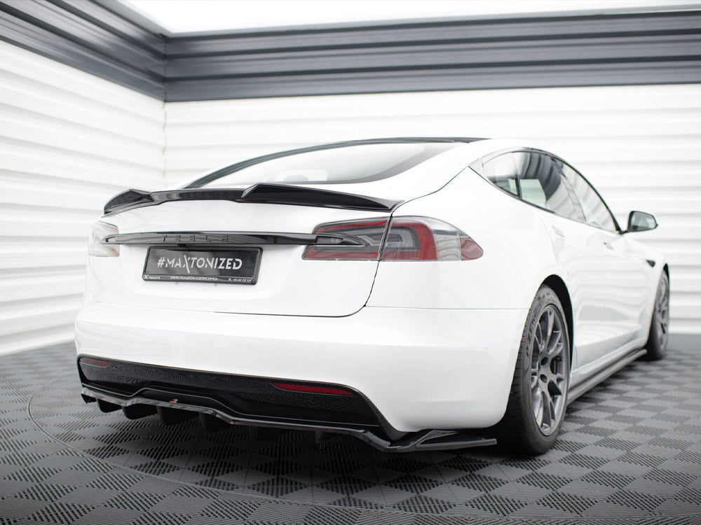 A white car with a sporty design is parked on a checkered floor. The back license plate reads "#MAXTONIZED." It's in a white, enclosed space with striped walls.