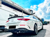 Car parked on a street next to a building under a clear blue sky. The white vehicle is a Mercedes CLA 250 4MATIC, with dual exhaust pipes and silver alloy wheels.