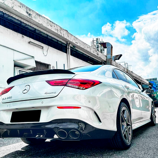 Car parked on a street next to a building under a clear blue sky. The white vehicle is a Mercedes CLA 250 4MATIC, with dual exhaust pipes and silver alloy wheels.