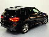 A black BMW X3 SUV stands parked in a brightly lit room. The car's rear lights are illuminated, highlighting its sleek design.