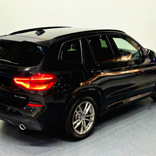 A black BMW X3 SUV stands parked in a brightly lit room. The car's rear lights are illuminated, highlighting its sleek design.