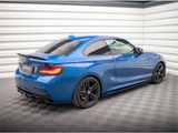 A blue sports car with black wheels is parked in a well-lit, enclosed showroom. The vehicle has a visible badge, 