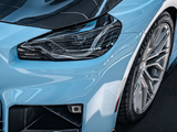 A light blue car's sleek front view, showcasing a detailed headlight, carbon fiber elements, and a Michelin tire in a glossy, clean indoor setting.
