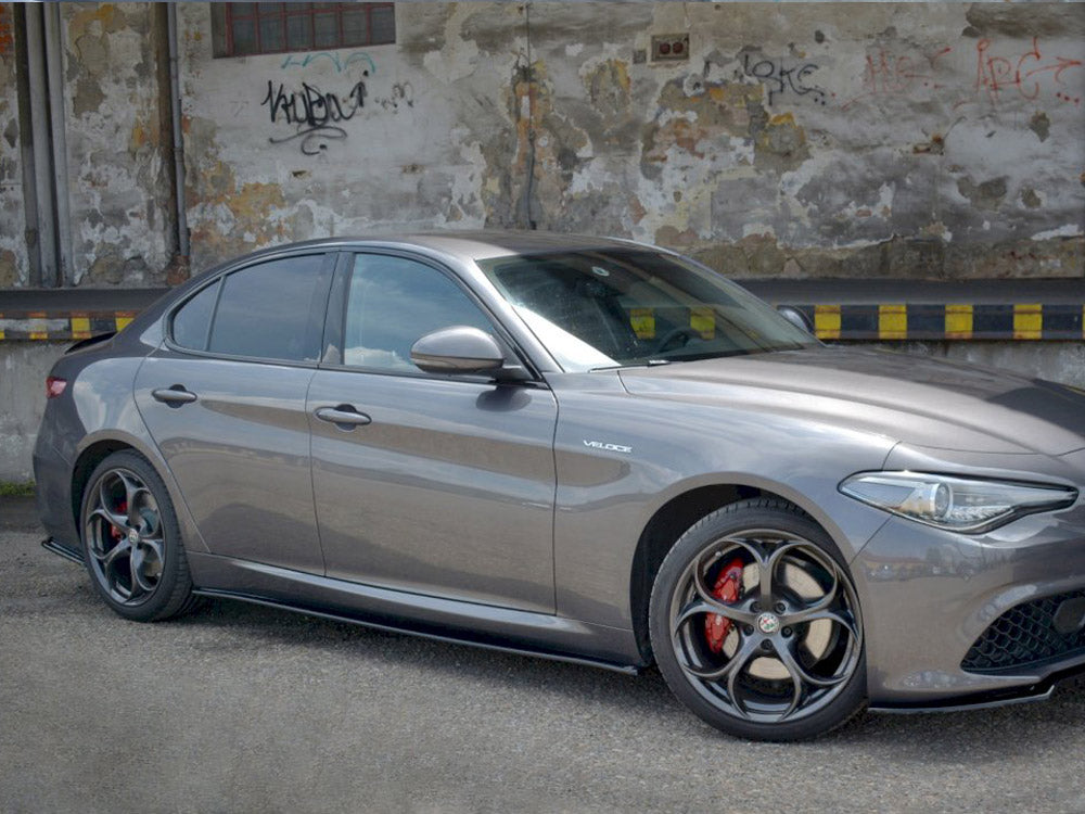 A silver car parked beside a weathered wall covered in graffiti and peeling paint. The ground is paved, and the word "VELOCE" is visible on the car's side.