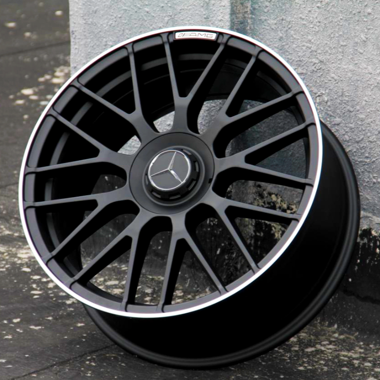 A black alloy wheel with a three-pointed star emblem rests against a textured wall. Text on the wheel reads "AMG," reflecting a sleek automotive design.