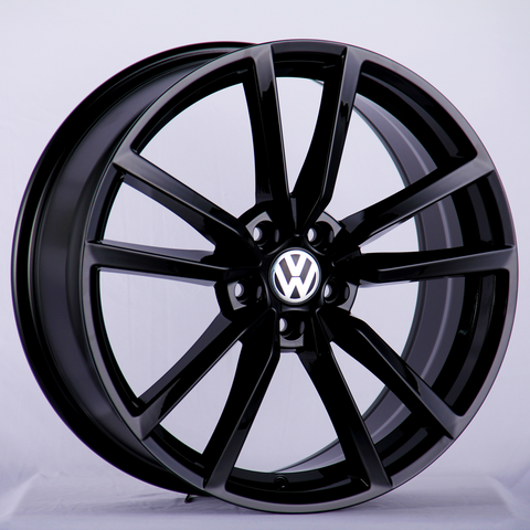 A glossy black alloy wheel featuring the Volkswagen logo at its center, positioned upright against a plain, light gray background.
