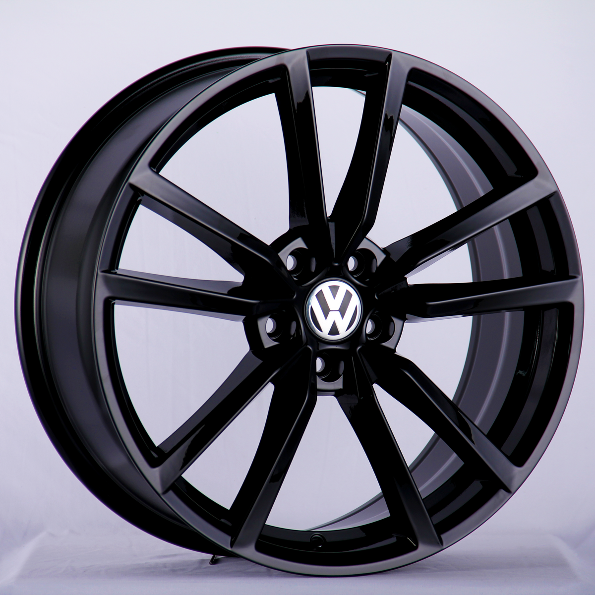 A black alloy wheel with a multi-spoke design displays the Volkswagen logo at the center, presented against a plain, light background.