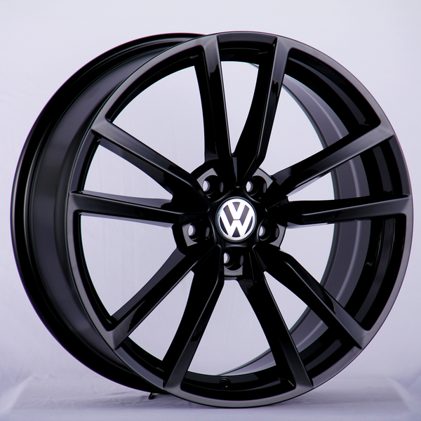 A black alloy wheel with a multi-spoke design displays the Volkswagen logo at the center, presented against a plain, light background.
