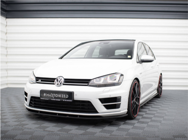 A white Volkswagen car, stationary on a checkered showroom floor, features a visible front grille and logo. Text on the license plate reads "#MAXTONIZED." The backdrop is a white, corrugated wall.