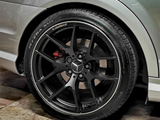 A black, multi-spoke car wheel with a Mercedes logo is stationary, set against a clean, tiled floor and silver vehicle body. Tire text reads: 