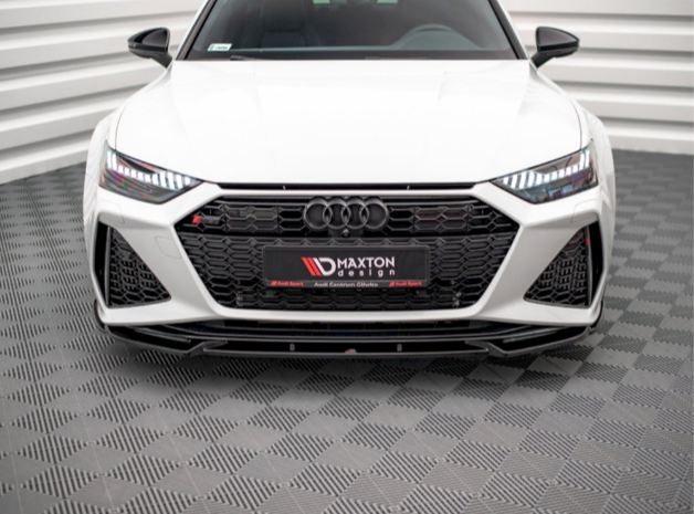 A white Audi car is stationary with its front visible, detailed with a prominent black grille and LED headlights. It is set in a white, patterned studio. Text: "MAXTON DESIGN."