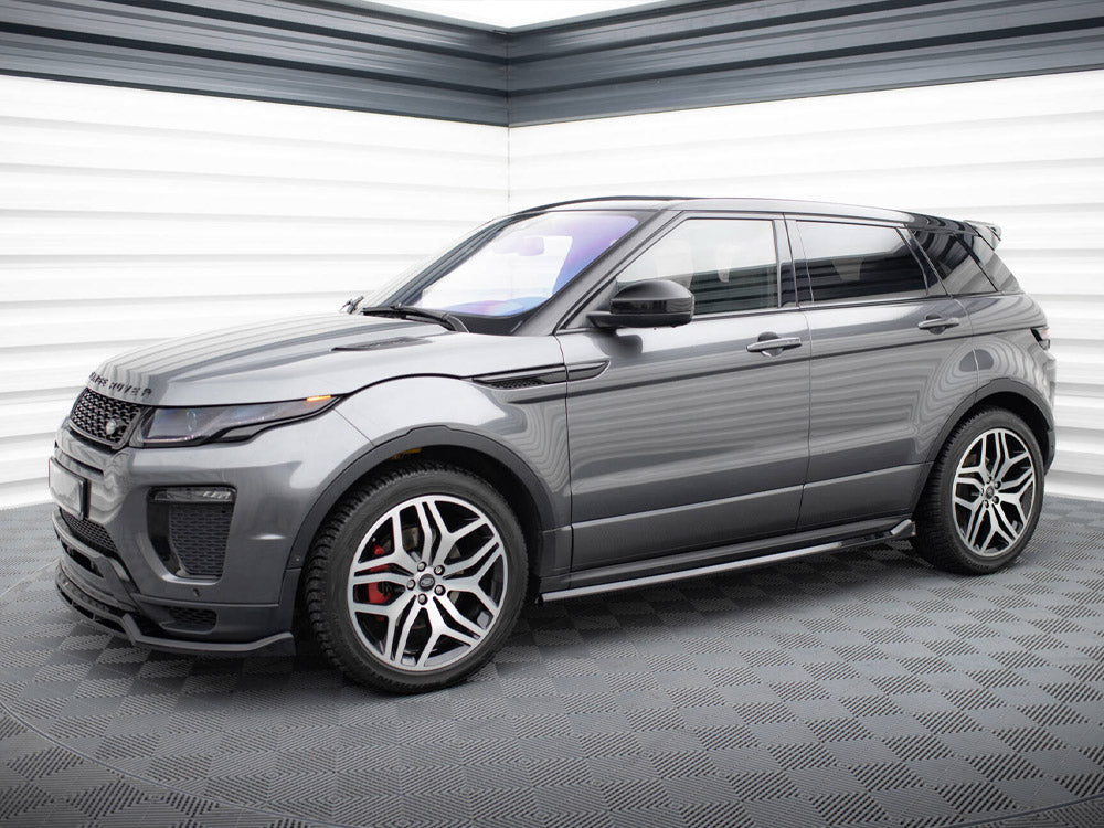 A sleek gray SUV with sporty rims is parked indoors on a textured floor, surrounded by striped white and gray paneled walls. The front displays "RANGE ROVER" on the hood.