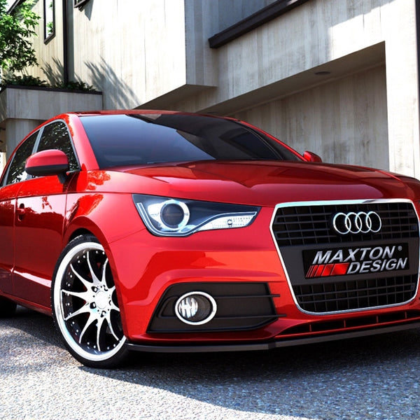 A red Audi car is parked on a sunlit street in front of modern buildings. The license plate reads "MAXTON DESIGN." Shadows and trees are visible nearby.