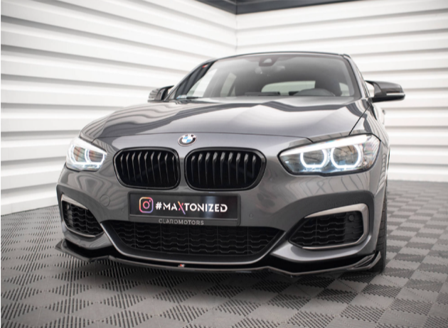 A gray BMW with illuminated headlights is parked in a modern, white, geometric garage. Text on the license plate reads "#MAXTONIZED" and "CLAROMOTORS."
