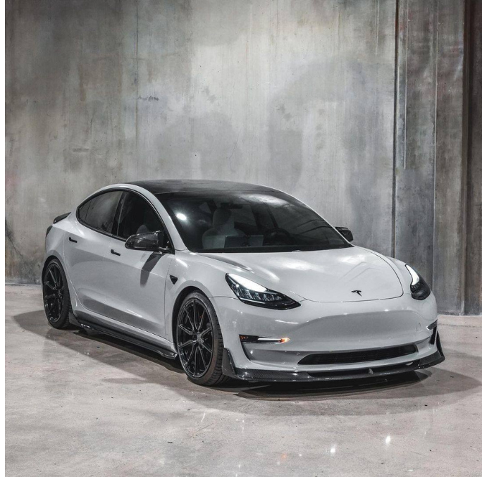 A sleek, white car with black wheels is parked in an industrial-style setting with plain, textured concrete walls and floor.