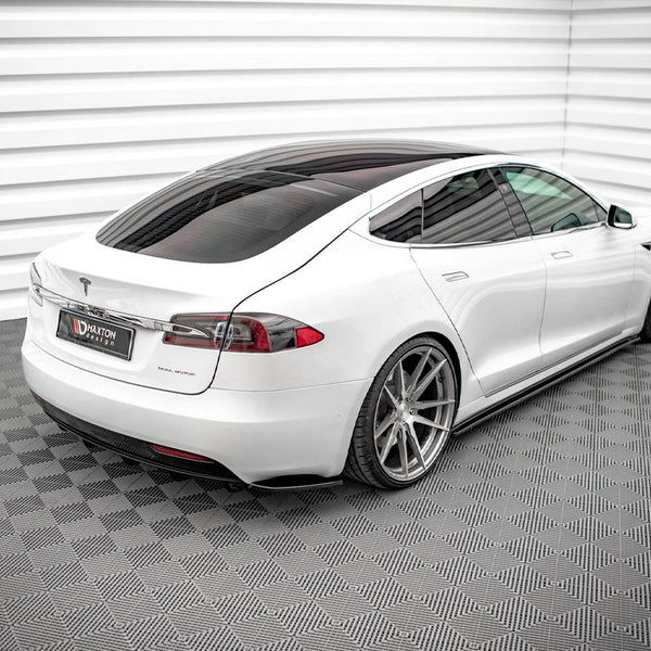A white car with tinted windows is parked in a room with textured flooring and ridged walls. A license plate displays the text "MAXTON DESIGN."