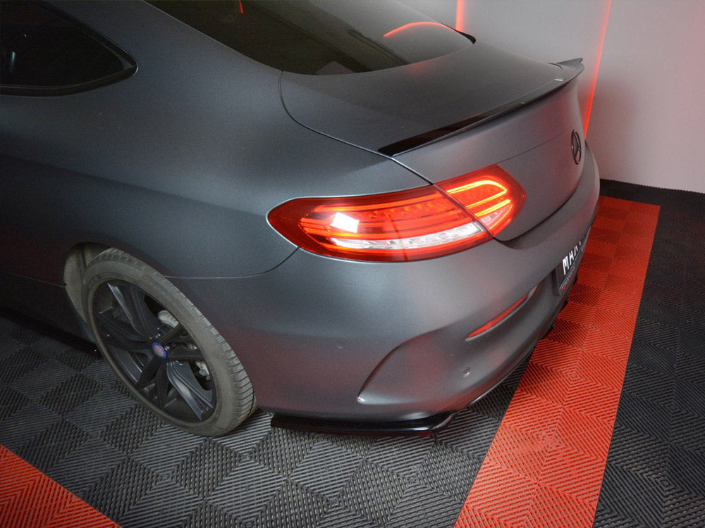 A matte black car with illuminated tail lights is parked on a black and red checkered floor in a well-lit indoor space.