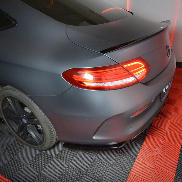 A matte black car with illuminated tail lights is parked on a black and red checkered floor in a well-lit indoor space.