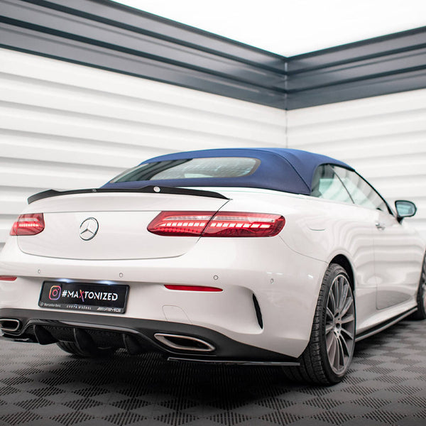 A white convertible car with a blue top parked in a bright, modern showroom with checkered flooring. Text on the license plate reads, “MaxTonized” with social media icon and AMG branding.