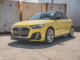A yellow Audi car parked on concrete, with black trim and a hexagonal grille, displays 