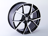 Stylish black and silver alloy wheel with a Volkswagen logo rests on a plain white background, showcasing its modern, angular spoke design.