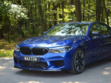 A blue car with sleek design stands parked on a shaded road, surrounded by dense green forest. The license plate reads 