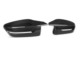Carbon fiber mirror covers are resting side by side; they have a sleek, glossy finish with a minimalist black-and-white design, set against a plain white background.