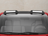 A red vehicle with a black roof features two rectangular, white-highlighted roof racks. The front windshield shows a steering wheel and gray seats inside the car, against a concrete background.
