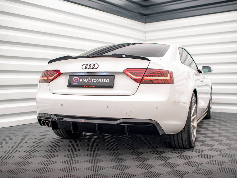A white Audi car is parked in a garage with patterned flooring and white walls. The license plate reads "#MAxtonized" with "Audi Sport" below it.