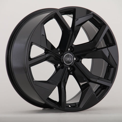 A glossy black alloy wheel with a five-spoke design and an Audi logo is displayed against a plain, light background.