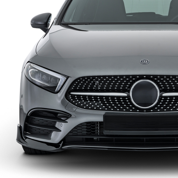 A gray luxury car is parked, showcasing its sleek front grille with a circular emblem. The vehicle sits in a well-lit studio environment, highlighting its polished exterior.