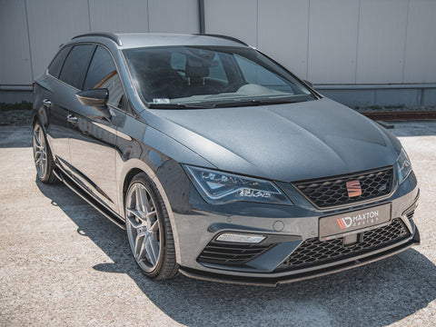 Car parked on concrete: A gray station wagon with tinted windows and alloy wheels is parked in a sunlit outdoor area. Text on the license plate frame reads, "MAXTON design."
