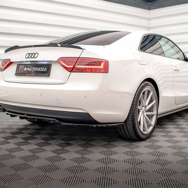 A white Audi coupe is parked, viewed from the rear in a stylish, modern garage with patterned flooring. The license plate reads "#MAXTONIZED" and features the Audi Sport logo.