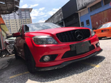 Red car parked on a street with a reflective black grille and black wheels. Surrounded by urban buildings and motorcycles under a partly cloudy sky. The car is positioned diagonally.