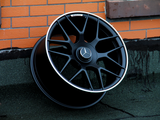 A black alloy wheel with a Mercedes logo rests against an orange brick wall. The wheel features intricate spokes and an 