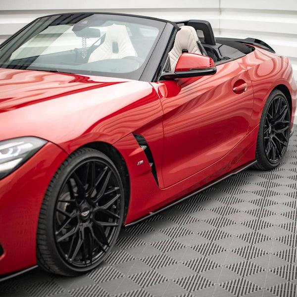 Red convertible sports car, parked with the top down, featuring sleek black wheels, in a bright, tiled space with geometric patterns on the floor and walls.