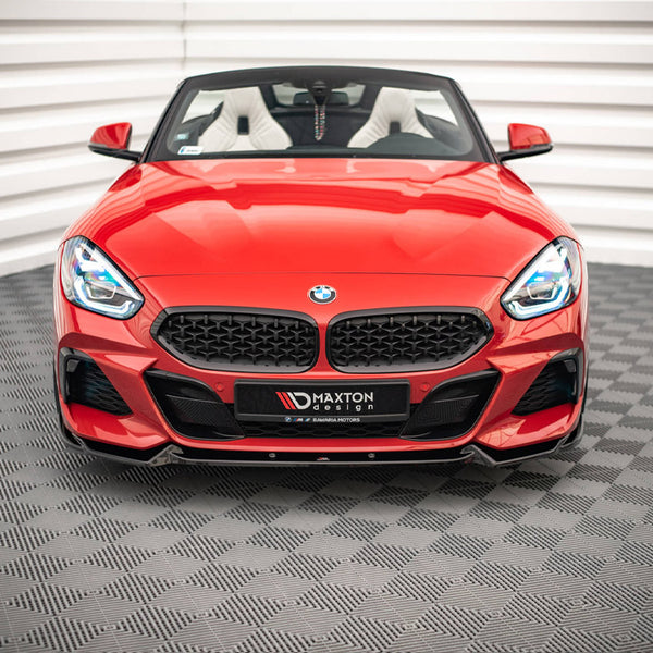 A red convertible sports car sits stationary on a patterned floor within a white-walled room. Its front grille prominently displays the BMW logo. Text on the bumper reads "MAXTON design."