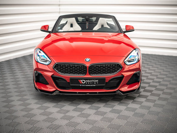 A red convertible sports car sits stationary on a patterned floor within a white-walled room. Its front grille prominently displays the BMW logo. Text on the bumper reads "MAXTON design."