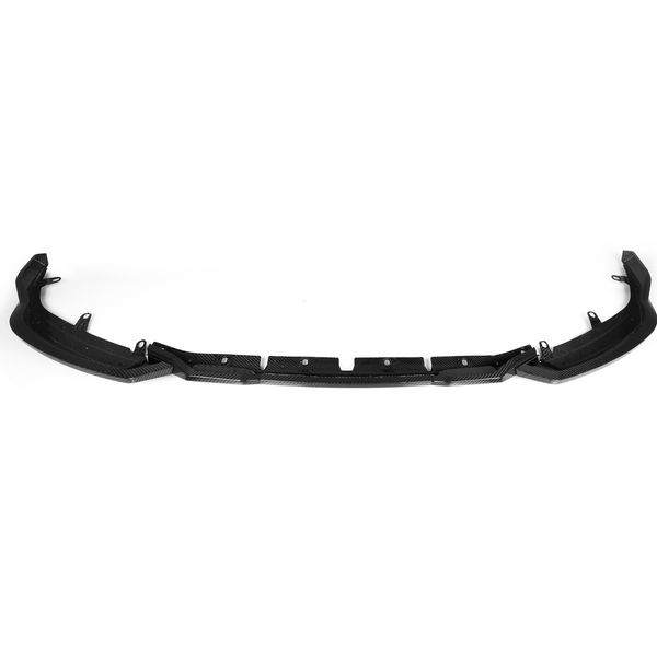 A black car bumper lip with small attachment points is laid flat against a plain white background, highlighting its sleek, curved design and textured surface.