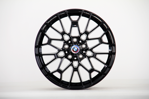 A black alloy wheel with a geometric spoke design, emblazoned with the BMW logo at the center, stands against a plain white background.