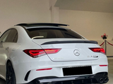 A white Mercedes-Benz CLA 45 AMG is parked indoors, showcasing distinct rear features, including dual exhausts and AMG badging. The setting includes a minimal, well-lit garage with decorative flowers.