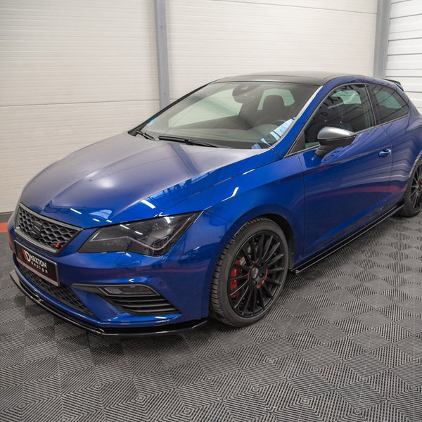 Blue hatchback car parked in a showroom with grey and red checkered flooring; features tinted windows, black alloy wheels, and a front grille. "Maxton Design" text visible on the front plate.